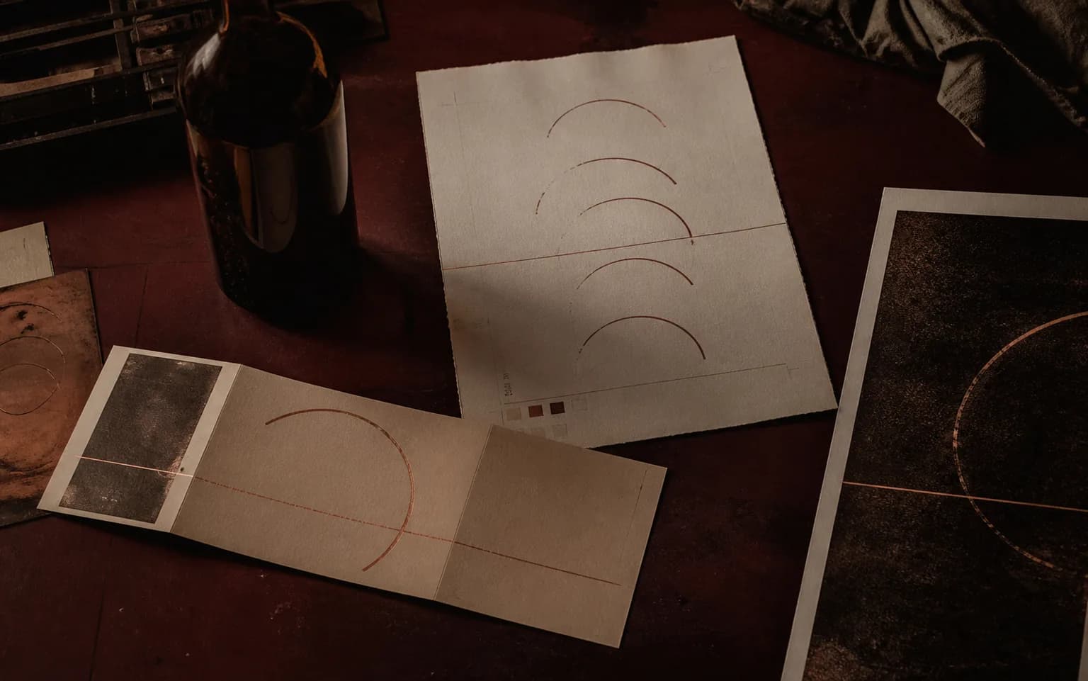 Halden Rye campaign proofs and an unlabelled amber bottle arranged on a dark oxblood printmaker's table.
